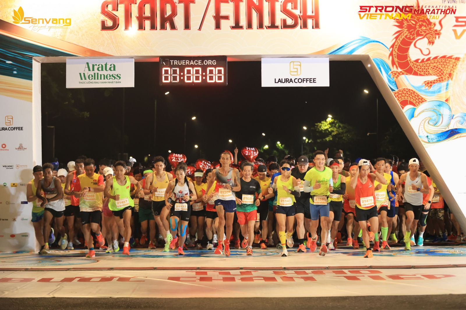 Runner lao qua cổng xuất phát trong đêm, đồng hồ TrueRace phía trên